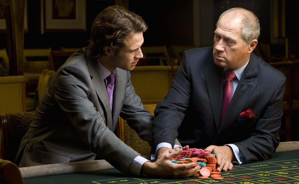 Older man gives younger man large pile of casino chips